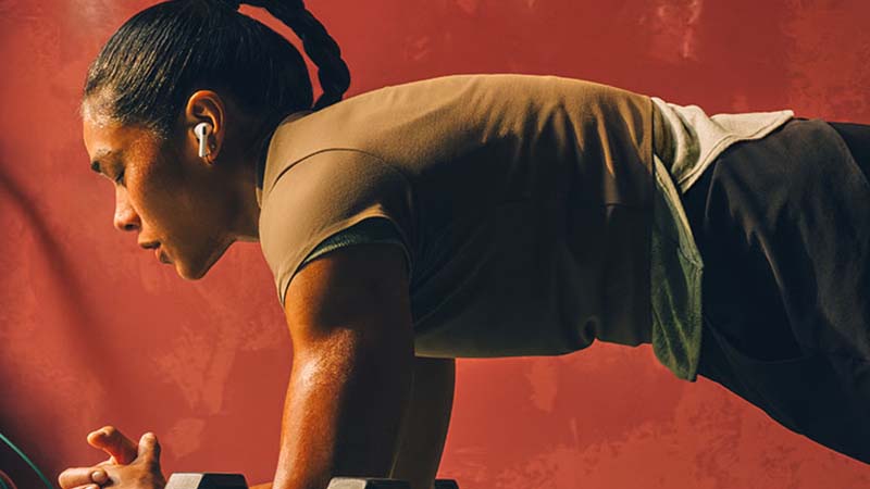 Mulher a fazer exercício e a usar uns Airpods Pro 3 da Apple, fundo vermelho