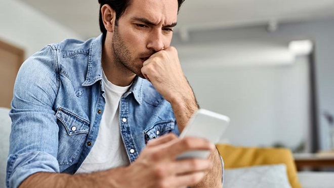 Homem a olhar para smartphone com preocupação devido a fraudes bancárias