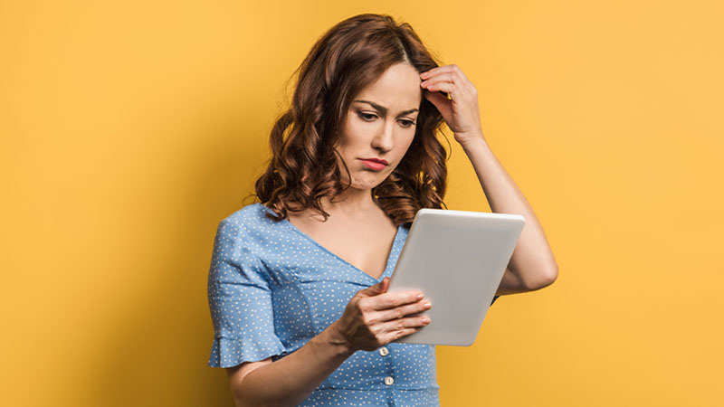 Mulher jovem com ar chateado a olhar para um tablet, fundo amarelo