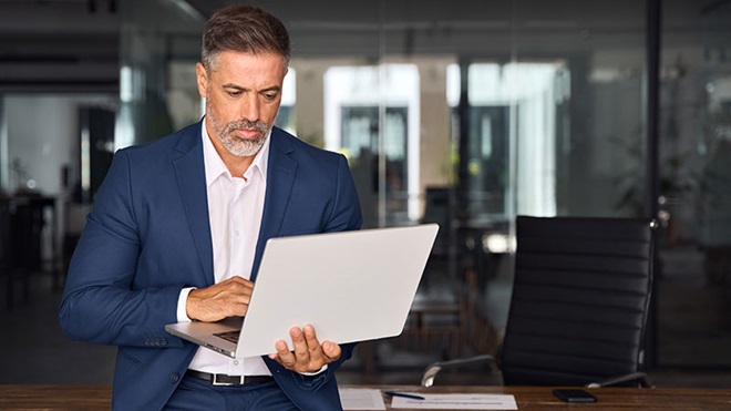Homem de negócios, no seu escritório, procura algo num portátil - alusão ao serviço cloud