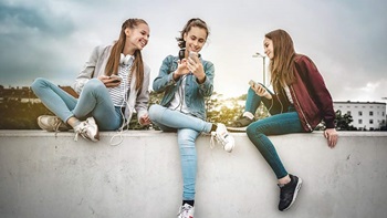 3 jovens sentadas em cima de um muro a ver os telemóveis