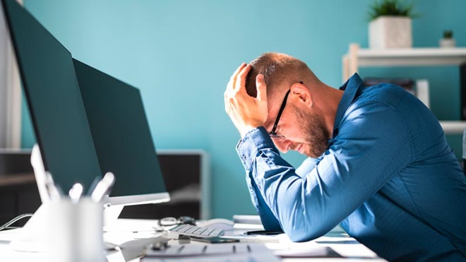 Homem a segurar a cabeça em frente a computadores - alusão ao cibercrime