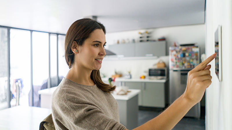 Mulher jovem numa cozinha mexe num aparelho inteligente