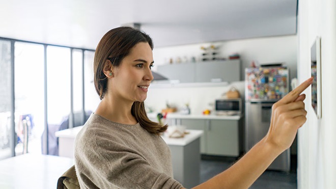 Mulher jovem numa cozinha mexe num aparelho inteligente