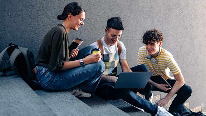 Grupo de três estudantes, numas escadas, com um portátil