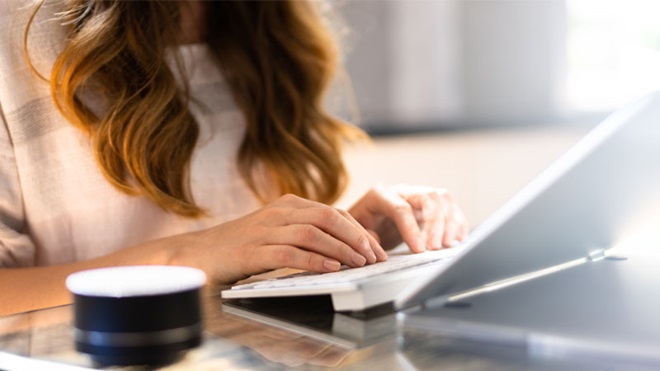 Mulher de cabelo comprido escreve num pequeno computador portátil branco sobre uma secretária