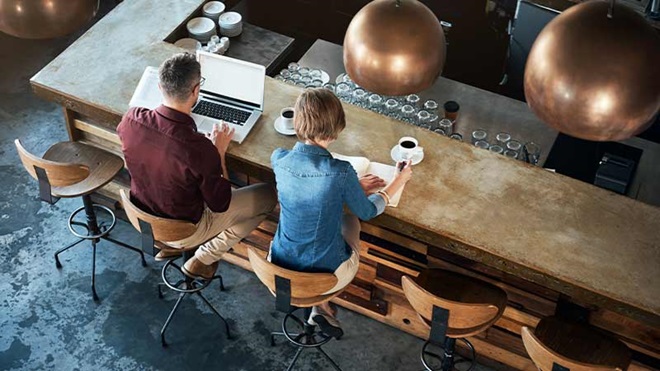 Homem a mulher de costas, sentados num café a trabalhar