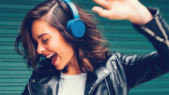 Mulher contente a dançar com auscultadores azuis.