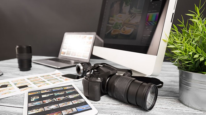 Máquina fotográfica, computador portátil, tablet com thumbnails, objetivas e provas de contacto sobre uma mesa de trabalho