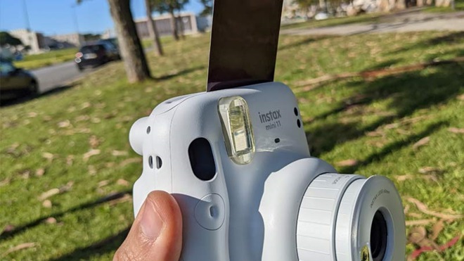 Pessoa a retirar fotografia instantânea de uma máquina fotográfica polaroid azul