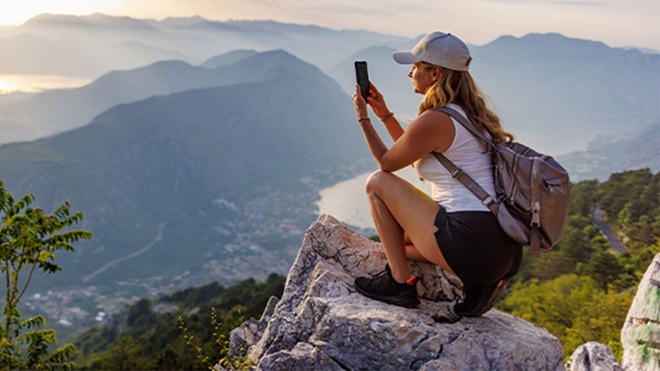 Mulher com mochila às costas a fotografar paisagem
