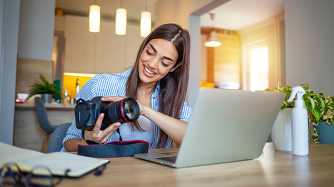Mulher com máquina fotográfica na mão a transferir fotografias para computador portátil