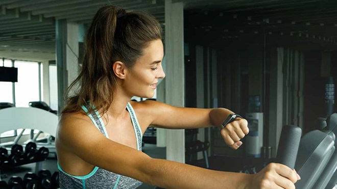 Plano aproximado de uma mulher jovem a consultar uma pulseira de fitness, numa máquina de um ginásio