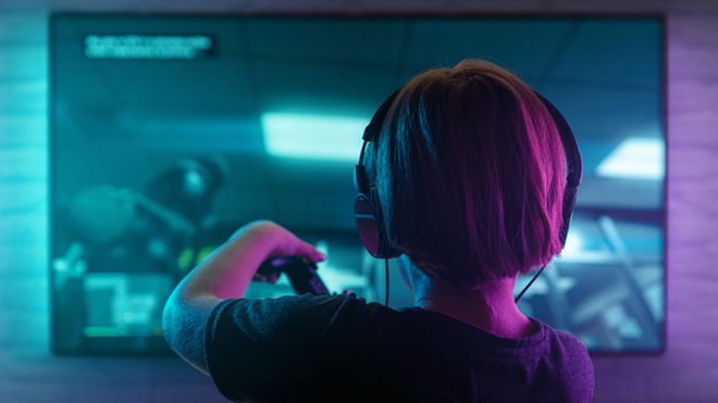 Criança em frente a um monitor, a jogar numa consola e com auscultadores na cabeça