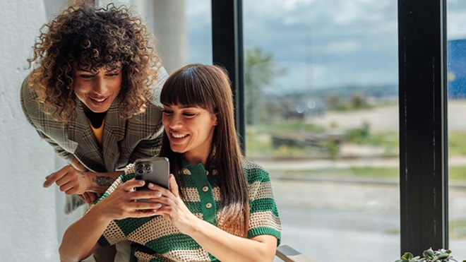 Duas mulheres jovens a consultar redes sociais no telemóvel 