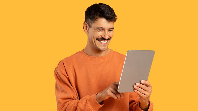 Homem de bigode a usar tablet, em fundo amarelo torrado, foto de estúdio