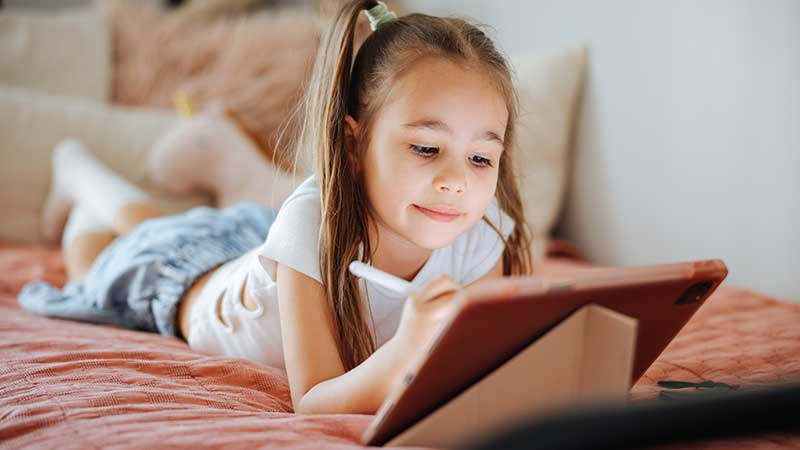 Criança deitada em cima da cama com um tablet