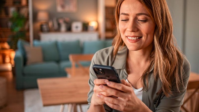 Mulher jovem com um telemóvel na mão, em casa