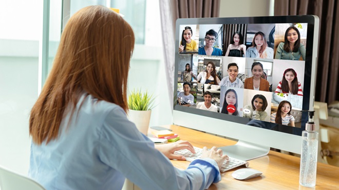 Mulher a trabalhar num computador e a assistir a uma videoconferência, com o frasco de álcool-gel em cima da mesa