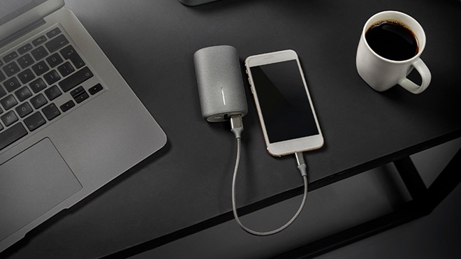 Powerbank ligado a um telemóvel, sobre uma mesa. Ao lado portátil e chávena de café