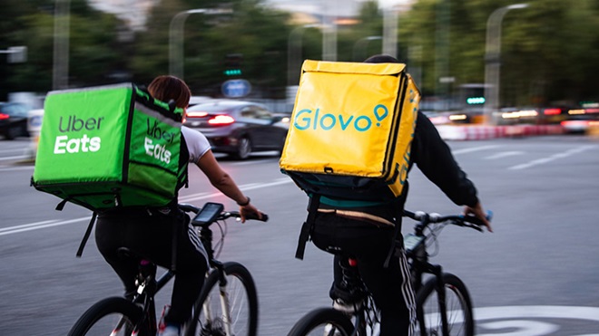 Duas pessoas de bicicleta com mochilas da ubereats e da glovo