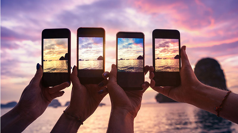 Quatro telemóveis levantados a fotografor pôr-do-sol