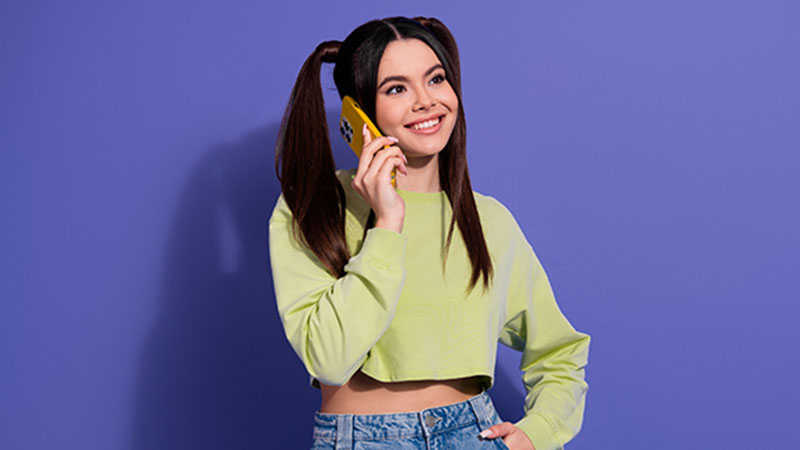 Jovem adulta morena e sorridente ao telemóvel, sobre fundo roxo