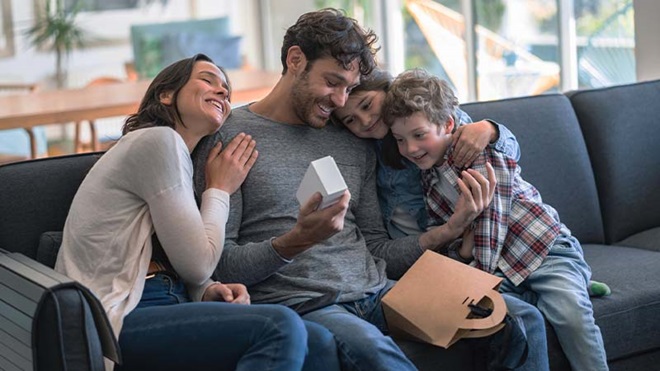 Família de quatro pessoas no sofá, dia do pai, pai recebe presente