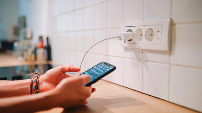 grande plano de alguém a segurar um smartphone ligado a uma tomada elétrica