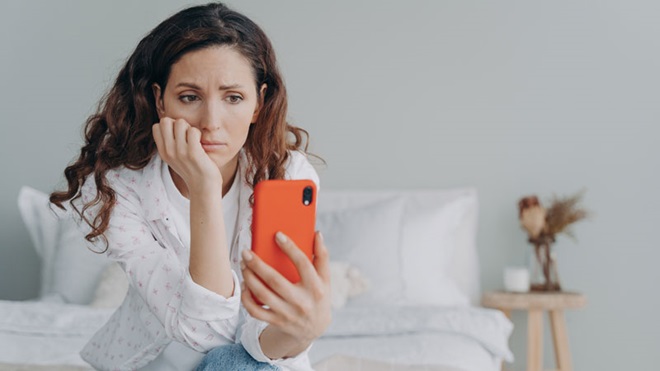 mulher observa telemóvel e suspeita de ataque de hacker