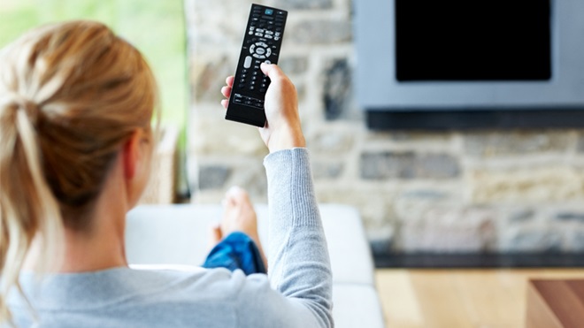 mulher sentada no sofá a ver televisão com o comando na mão