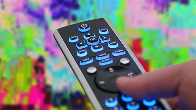 mão a pressionar comando de televisão para sintonizar canais de TDT