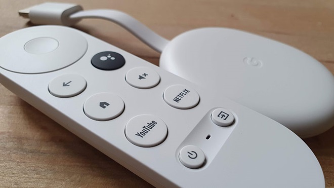 Chromecast com Google TV, sobre uma mesa de madeira, acompanhado pelo telecomando fornecido de origem