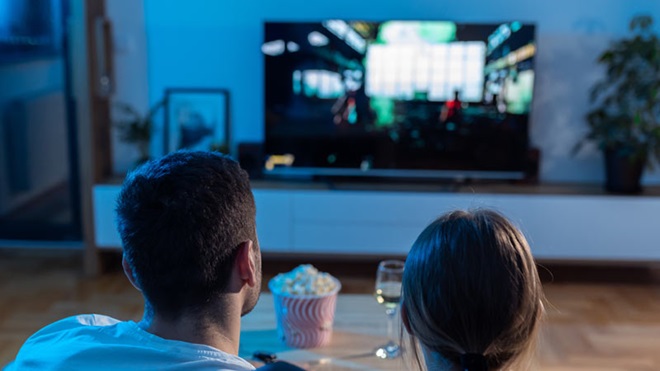 Casal a ver televisão e balde de pipocas