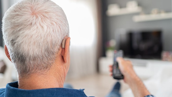 Homem com aparelho auditivo a ver televisão