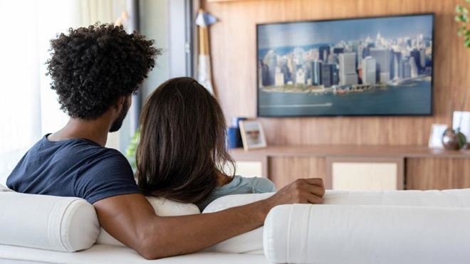 Casal sentado num sofá, de costas, a ver televisão na sala
