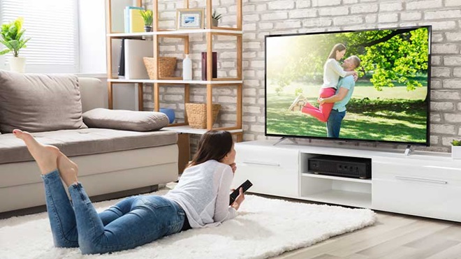 Mulher vê televisão deitada na sala