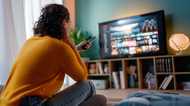 Mulher jovem sentada no chão com o comando da TV na mão